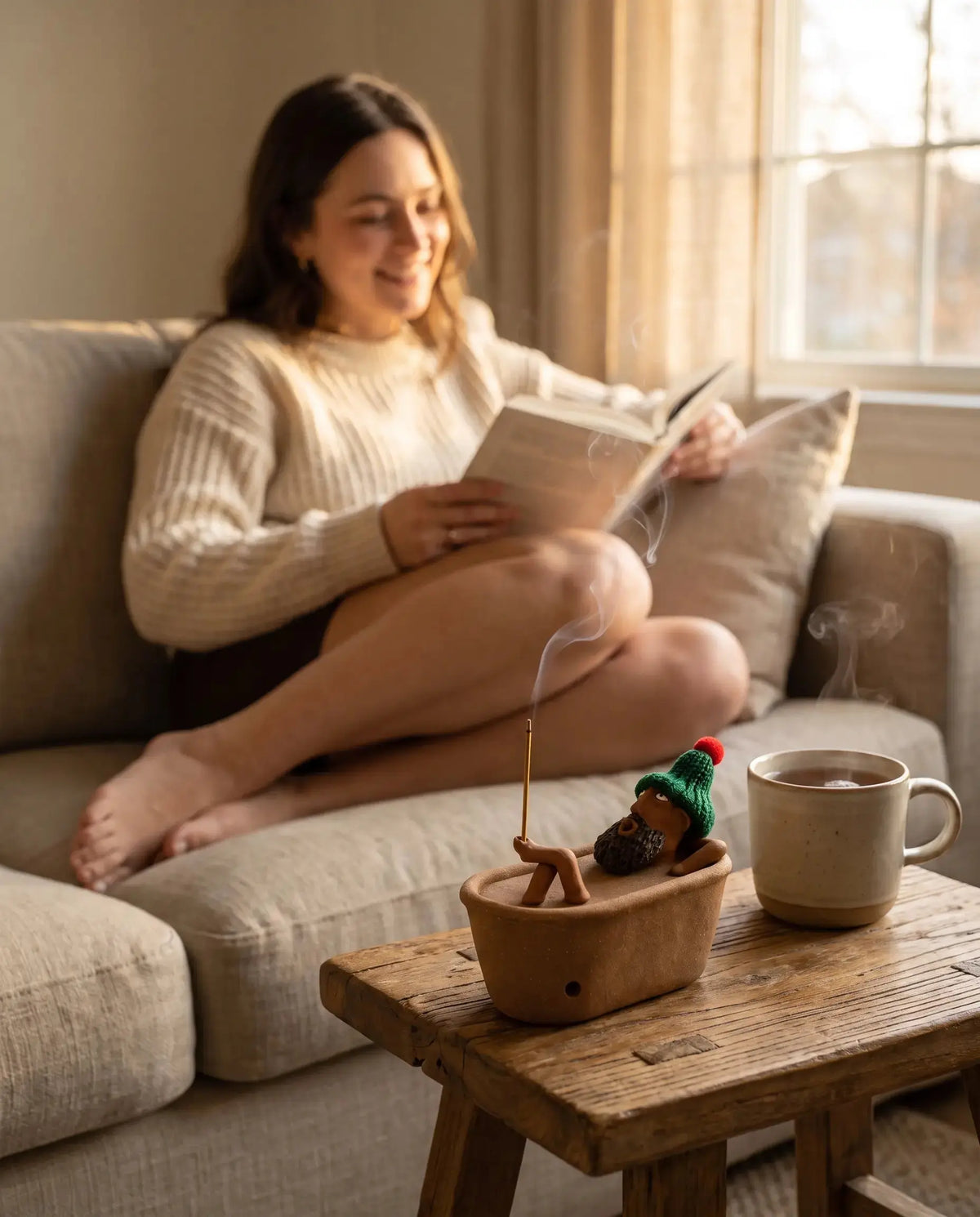 Woman reading on the sofa beside the Lazy Bath Man incense burner
